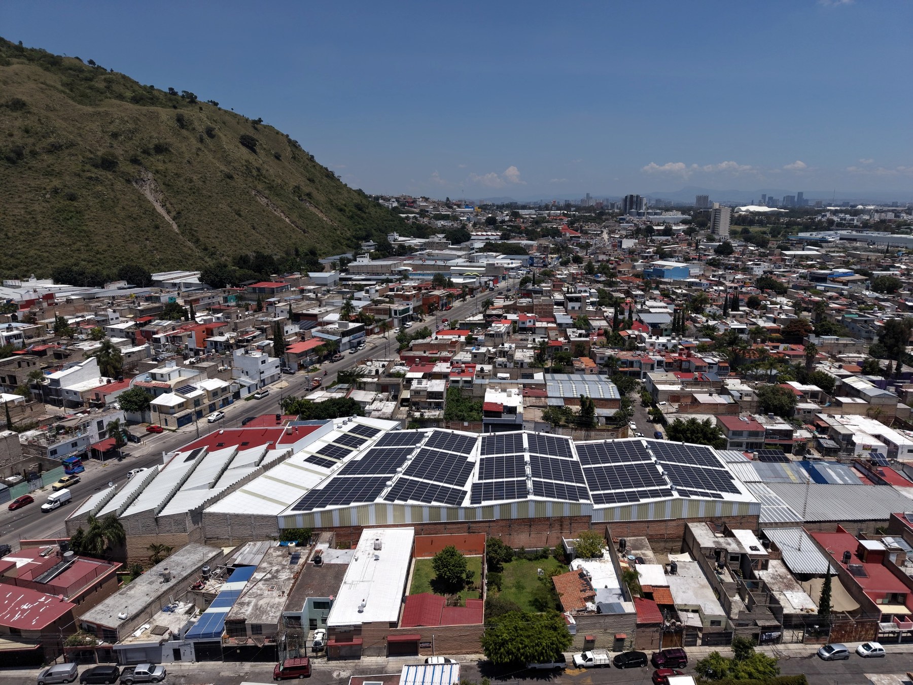 Vista aérea de la nave con cubierta fotovoltaica, al pie del Cerro del Colli y con el poniente de Guadalajara al fondo