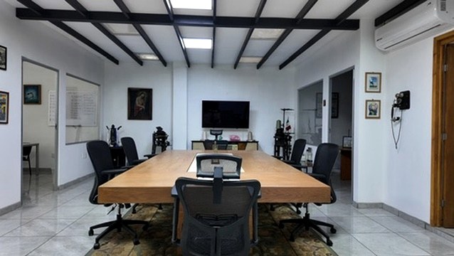Sala de juntas con mesa larga, pantalla y estructura de vigas a la vista